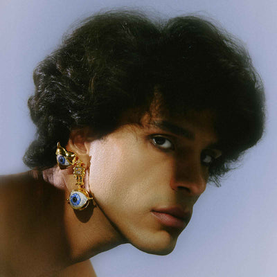 Close-up of a person wearing large, ornate earrings with a light blue background